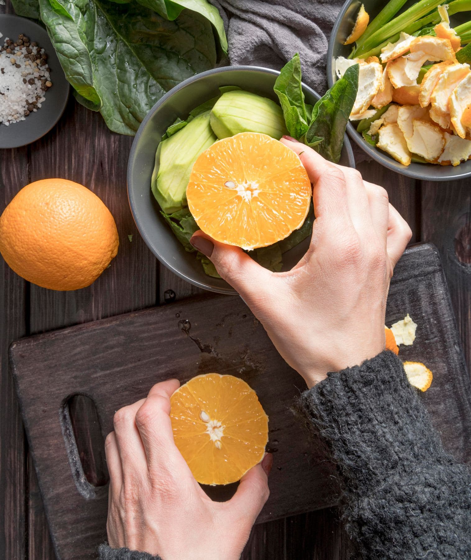Manos exprimiendo naranjas junto a una ensalada verde